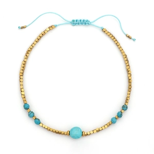 Detailopname van geweven boho-armband met turquoise kralen en gouden kubussen op wit