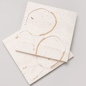 Detalle de pulseras de cuentas blancas y cilindros dorados sobre piedra beige