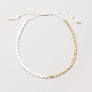 Detalle de una pulsera bohemia hecha a mano con cuentas doradas y cordón de cera blanco