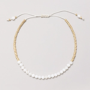 Detalle de una pulsera bohemia con cuentas blancas y cuentas de metal dorado