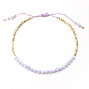 Detalle de pulsera de cuentas moradas claras con espaciadores dorados y cordón ajustable