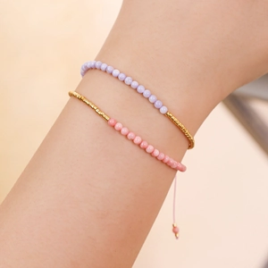 Detalle de pulseras bohemias de cuentas en rosa y lila con cierre de cordón ajustable