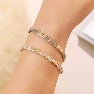 Detail of bohemian Tila bead bracelets in green and pink on wrist with gold accents