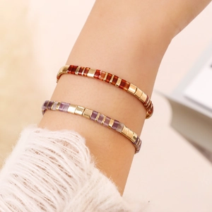 Close-up of stacked red-brown and lavender Tila bead bracelets with gold accents