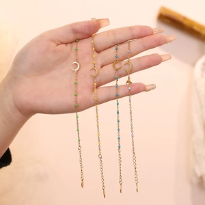 Detail of four gold moon bracelets with colorful beads held by a hand in warm lighting