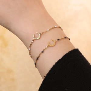 Detail of a gold moon crescent charm bracelet with black and white beads on a wrist