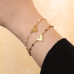 Dettaglio di ciondoli a cuore dorati su bracciali a catena sottile con perline bianche e nere