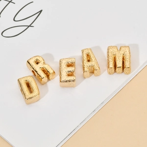Makroaufnahme vergoldeter Kupfer-Buchstabenperlen mit Hammerschlag-Textur für DREAM