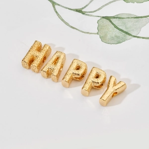 Makroaufnahme goldener DIY-Perlen mit HAPPY-Schriftzug und Hammerschlag-Textur