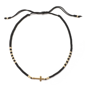 Detalle de pulsera de cuentas negras con dije de cruz dorada y cordón ajustable