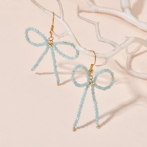 Detail of light blue beaded bow earrings on a white coral display stand in warm light