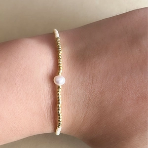Detalle de pulsera Miyuki de cuentas doradas con perla blanca ajustable en la muñeca
