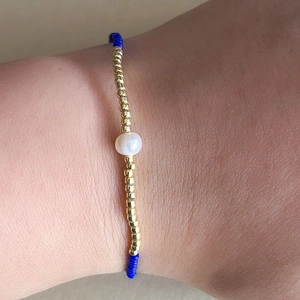 Detalle de una perla blanca con cuentas azules y doradas en pulsera elástica fina
