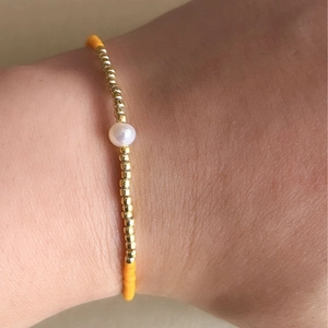 Detalle de pulsera de cuentas con cuentas doradas, cuentas naranjas y una perla