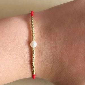 Detalle de la pulsera hecha a mano con cuentas doradas, rojas y una perla blanca central