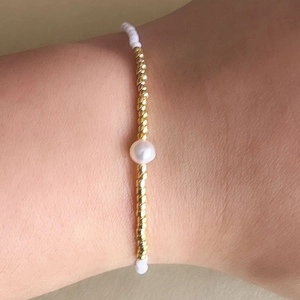 Detalle de la pulsera elástica con cuentas blancas, perlas y cuentas doradas rizadas
