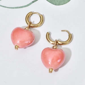 Pink heart-shaped ceramic drop earrings with gold hoops on a minimalist background