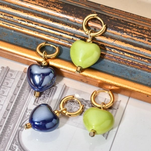 Detailed view of light green and dark blue ceramic heart pendants on gold hoop earrings