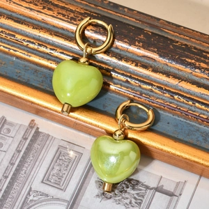 Close-up of light green heart ceramic earrings with gold metal hoops on vintage wood