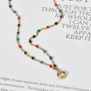 Gedetailleerde close-up van een gouden rvs ketting met kleurrijke kralen en zirkoon hanger