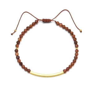 Detail eines Edelsteinarmbands mit goldfarbenem Rohr und verstellbarer Schnur