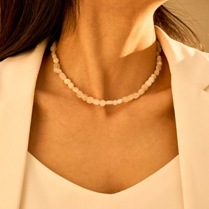 Detailopname van een bohemien witte edelsteenketting gedragen met een witte blazer