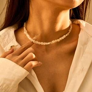 Detail van een boheemse ketting van witte halfedelstenen gedragen in warm avondlicht