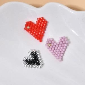 Three handmade beaded heart charms in red, purple, and black MIYUKI beads on white ceramic tray