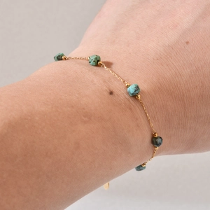 Gold stainless steel link bracelet with natural green stone beads on a woman's wrist