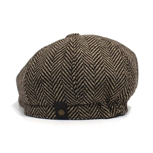 Dettaglio del cappello baker boy a spina di pesce con cinturino in pelle e bottone metallico