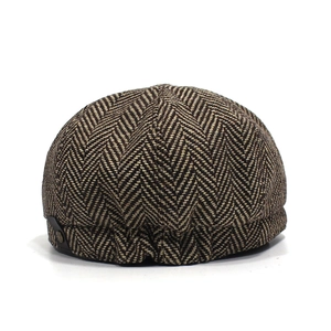 Dettaglio del berretto newsboy in tweed a spina di pesce con bottone in metallo ed elastico