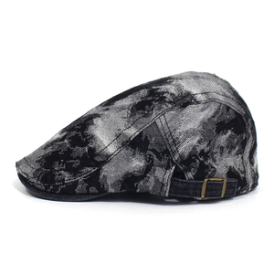 Detail view of washed denim flat cap showing ink wash pattern and bronze metal buckle