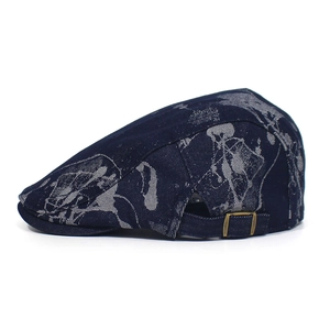Detail view of the bronze metal adjustment buckle on the dark blue denim flat cap