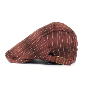 Détail du béret rayé marron-rouge montrant le tissu texturé et la boucle en bronze