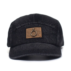 Detail view of washed denim 5-panel baseball cap with metal ring on brown patch