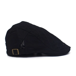 Detail view of black cotton flat cap featuring quilted patterns and bronze metal buckle