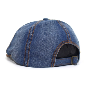 Detail of blue washed denim octagonal cap with brown stitching and adjustable metal buckle