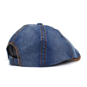 Detail view of denim newsboy cap showing brown double stitching and adjustable bronze buckle