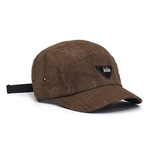 Close-up of brown checkered camper hat featuring a black triangle label and metal eyelet