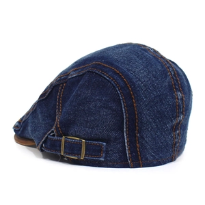 Close-up of vintage blue denim flat cap showing washed texture and bronze metal buckle