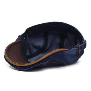 Detail of dark blue denim beret with brown leather brim and metal side adjustment buckle