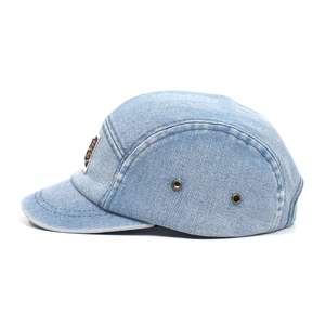 Detailed close-up of light blue washed denim camper hat with metal eyelets and logo tag