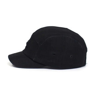 Close-up of black five-panel camper hat with metal eyelets and a woven side label