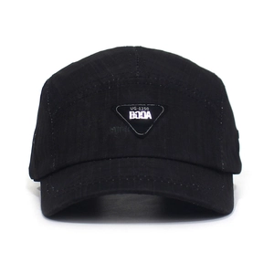 Macro detail of black textured baseball cap featuring a triangular metal logo plate