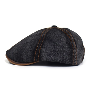 Detail view of denim flat cap with orange stitching and brown leather trim on visor