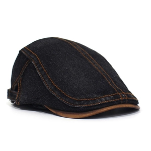 Detail of black denim flat cap with contrast orange stitching and brown leather brim