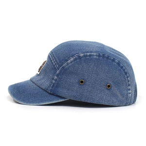 Detail of washed denim camper cap featuring vintage metal eyelets and a square metal logo