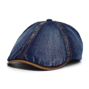 Detailed view of dark blue washed denim newsboy cap with brown leather brim and contrast stitching