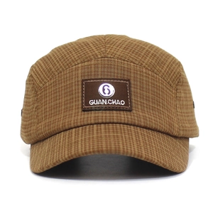 Detail van een bruine geruite 5-panel camp pet met een rechthoekig merklabel erop