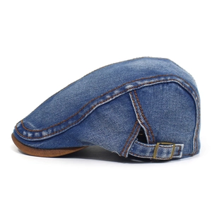 Detail view of denim flat cap showing orange stitching and brown faux leather brim